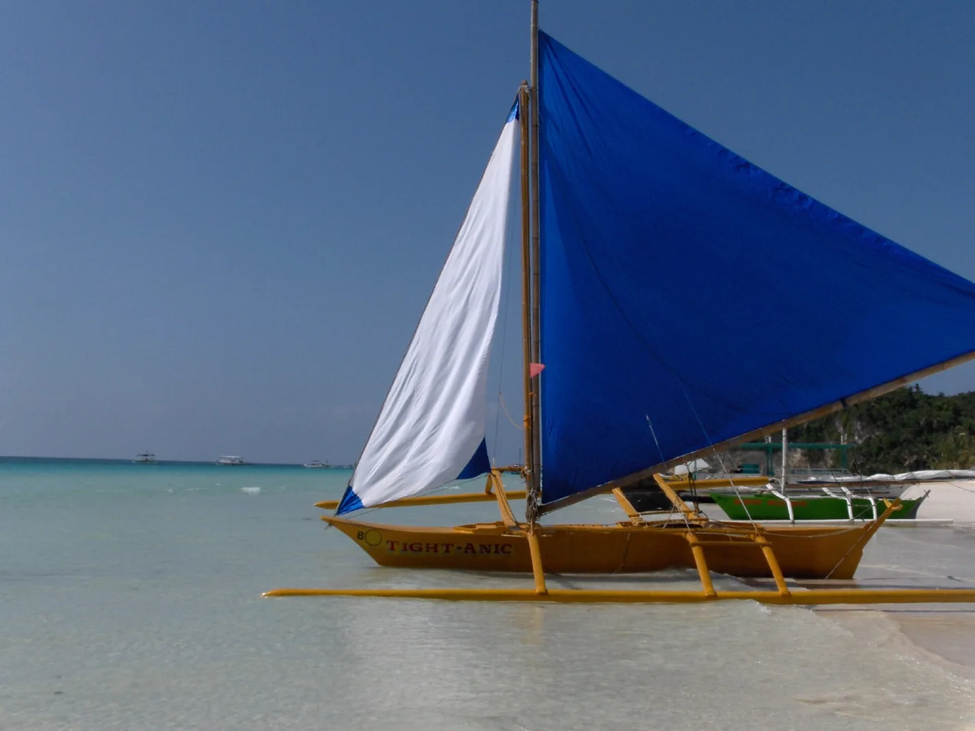 Wide view of Boracay's White Beach shoreline seen from the water on a clear afternoon, with pale sand and resort buildings visible