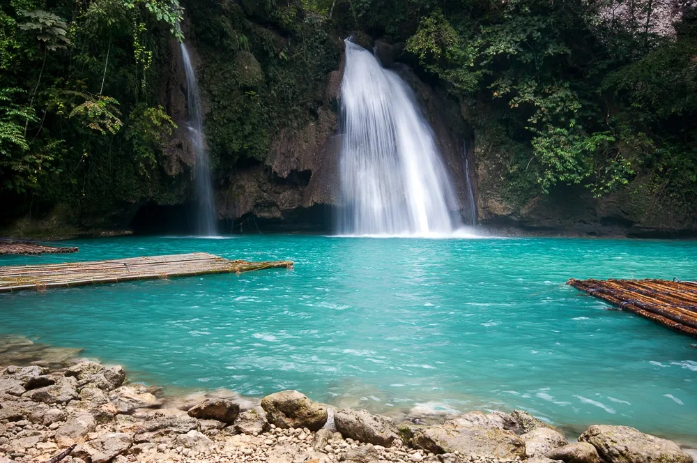 The main pool of Kawasan Falls first tier with bamboo rafts and turquoise travertine water