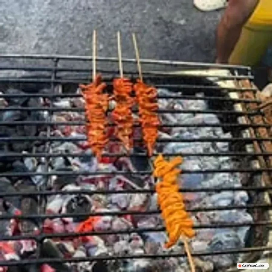Street vendor grilling skewers on an open charcoal grill